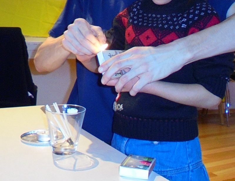 Mit helfenden Händen wird das Anzünden eines Streichholzes und einer Kerze geübt.